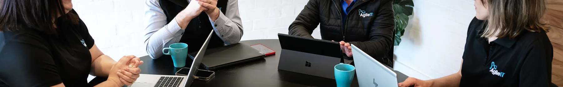 The Agile IT team working together around a table with laptops, Microsoft Surface devices and coffee
