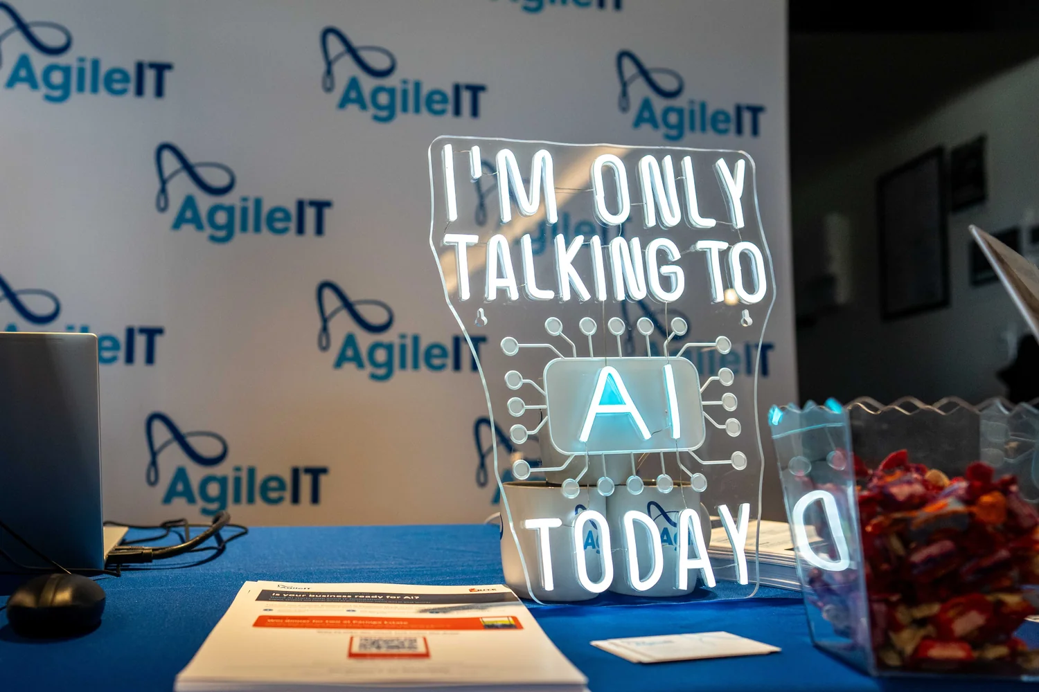 The "I'm only talking to AI today" sign on the Agile IT stand at the B.I.T.E Business Conference 2026, beside flyers asking whether your business is ready for AI.