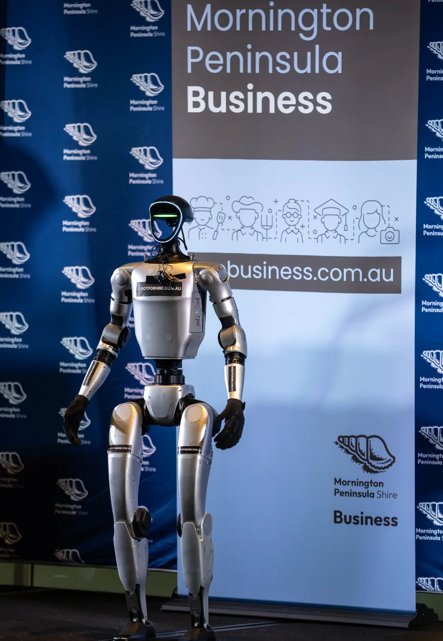 A humanoid robot standing on stage in front of the Mornington Peninsula Shire business backdrop at the B.I.T.E Business Conference 2026.