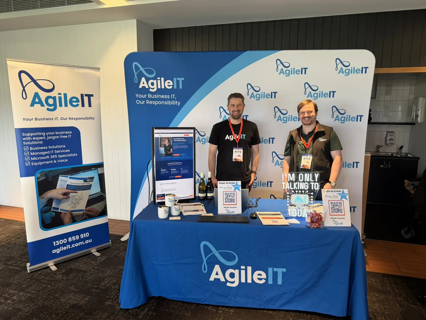 The Agile IT stand at the B.I.T.E Business Conference 2026, two team members with the branded backdrop, the Paringa Estate dinner-voucher prize draw and an I am only talking to AI today neon sign.