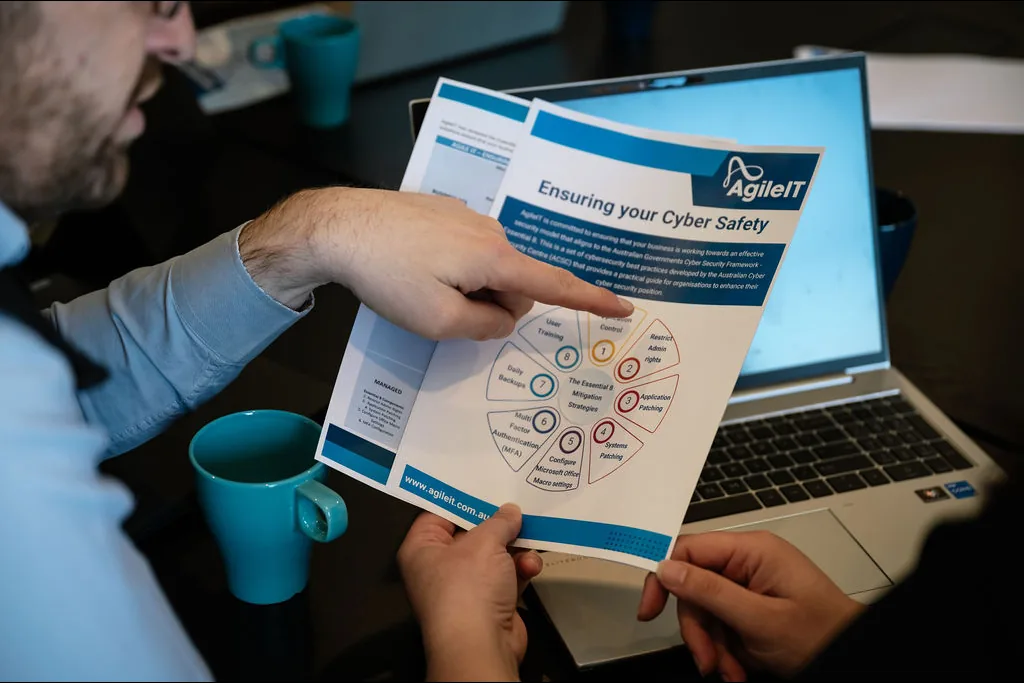 An Agile IT adviser pointing to a cyber safety guide beside a laptop during a client conversation