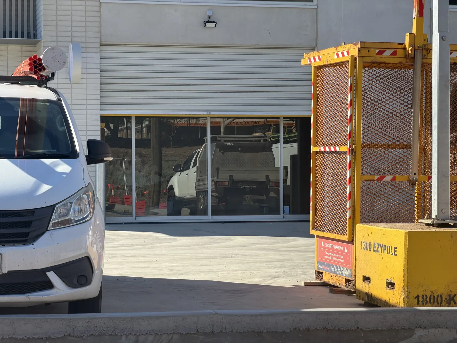 Construction-phase exterior shot, work vehicles, lift platform, roller shutters partly up