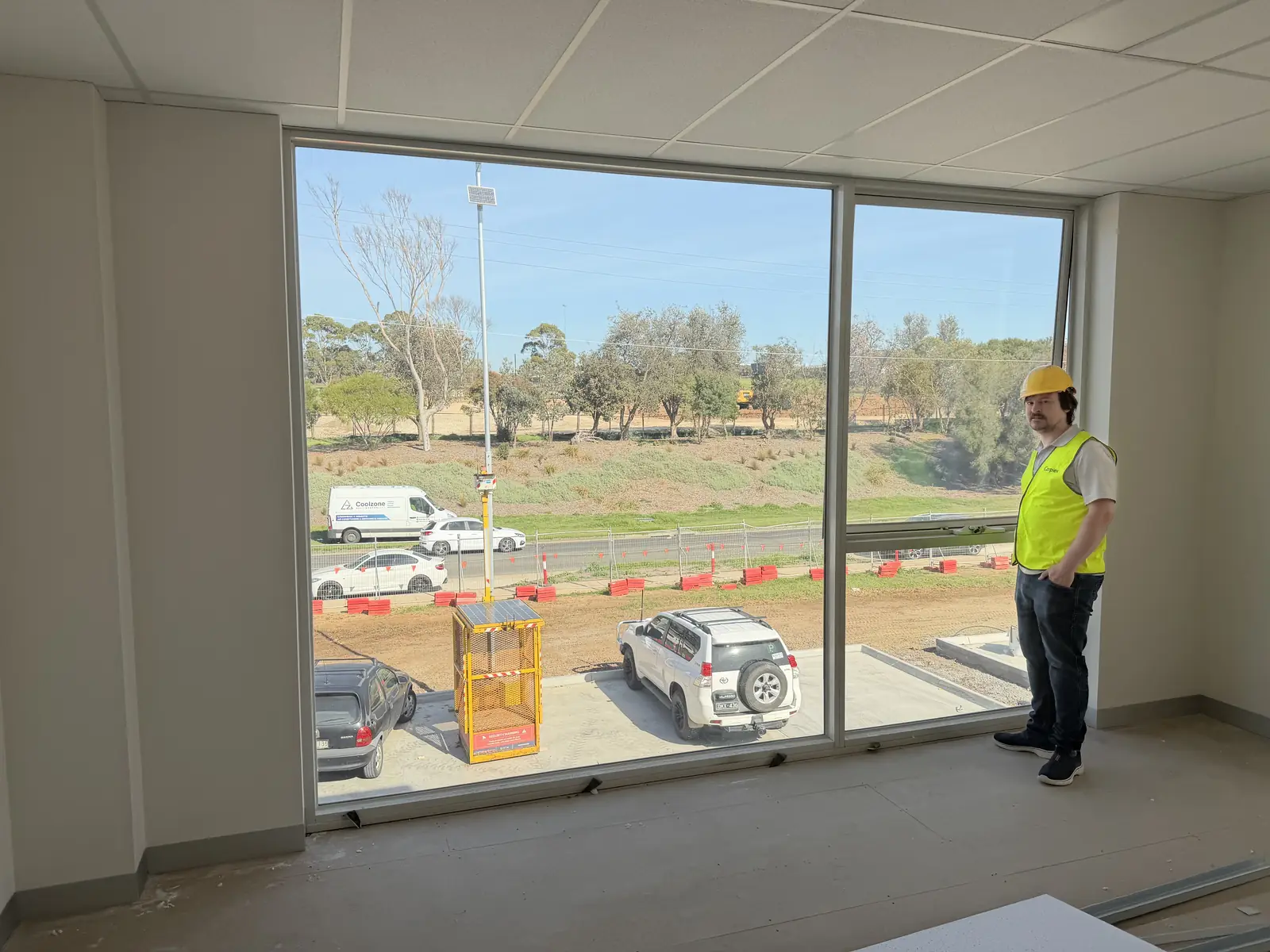 Looking out from inside the new office during fit-out, high-vis hat, large window, view of construction site outside
