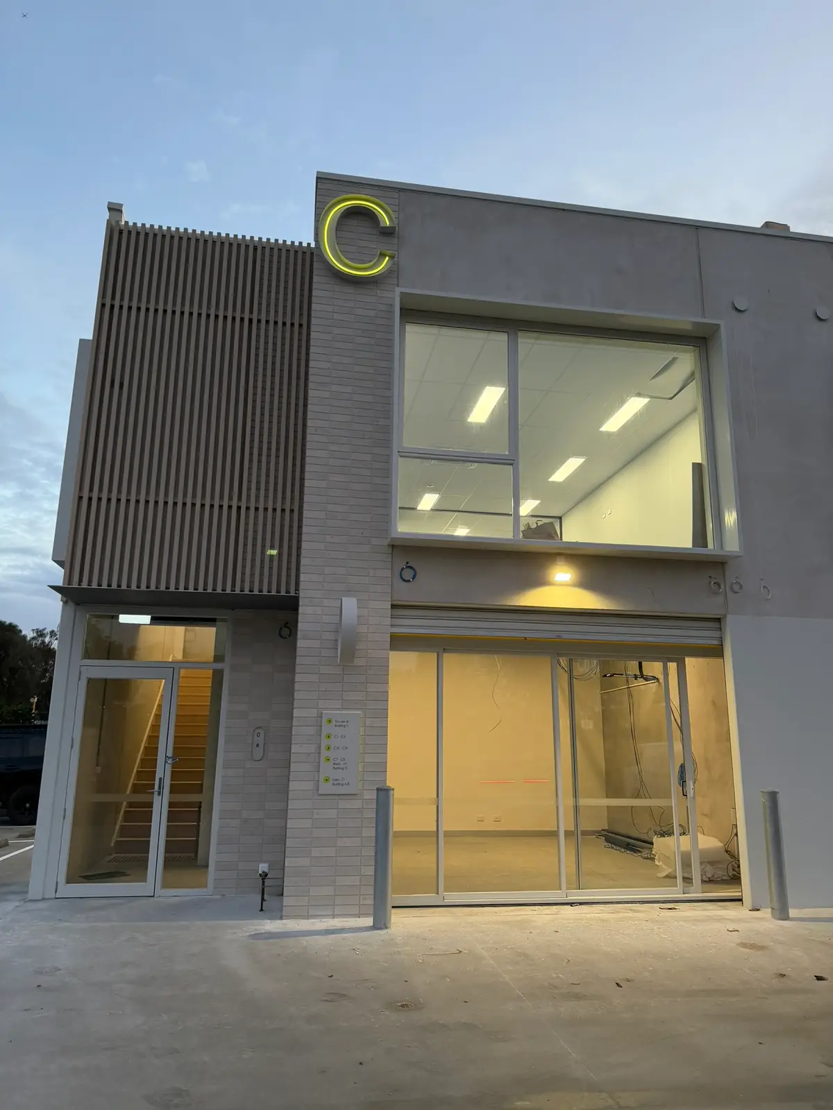 The illuminated C signage above the Building C entrance at Free Form, Mornington, glowing at dusk with the fitted-out interior visible through the glass