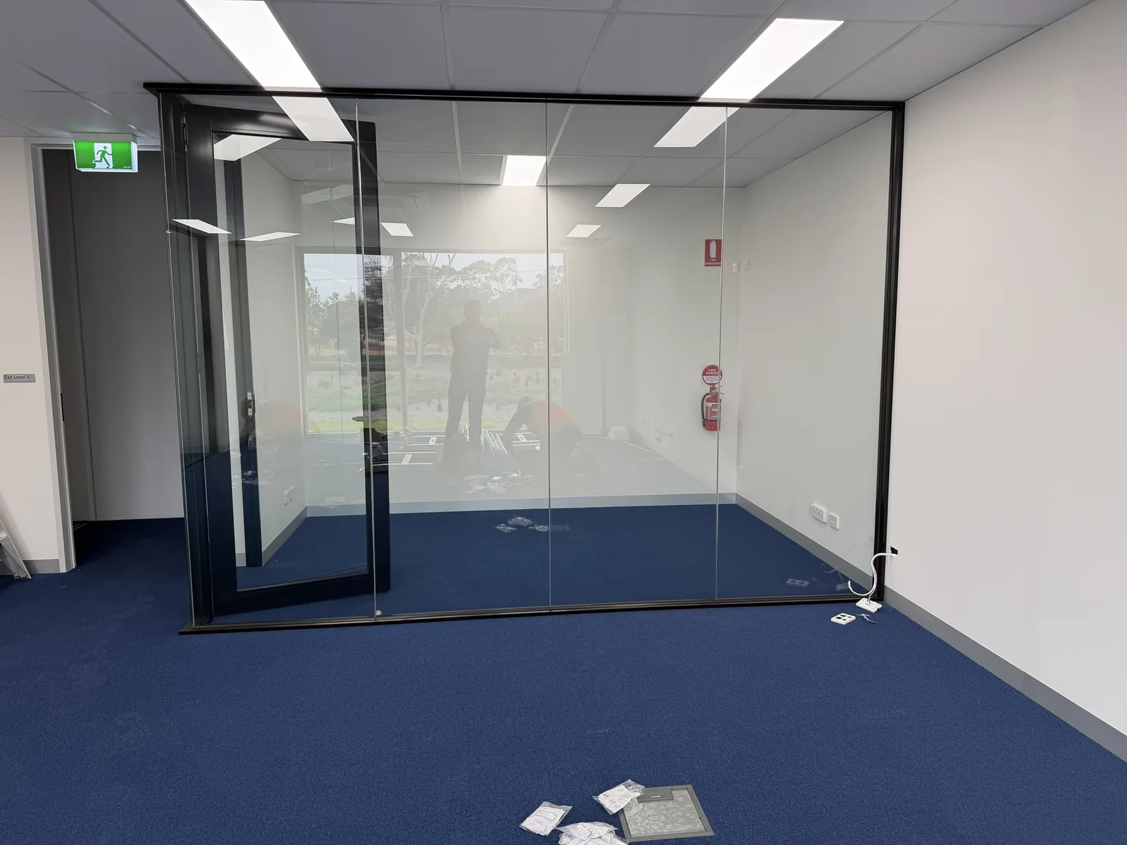 A glass-partitioned private office upstairs at Free Form, Mornington, black-framed glass walls and door, blue carpet, during fit-out