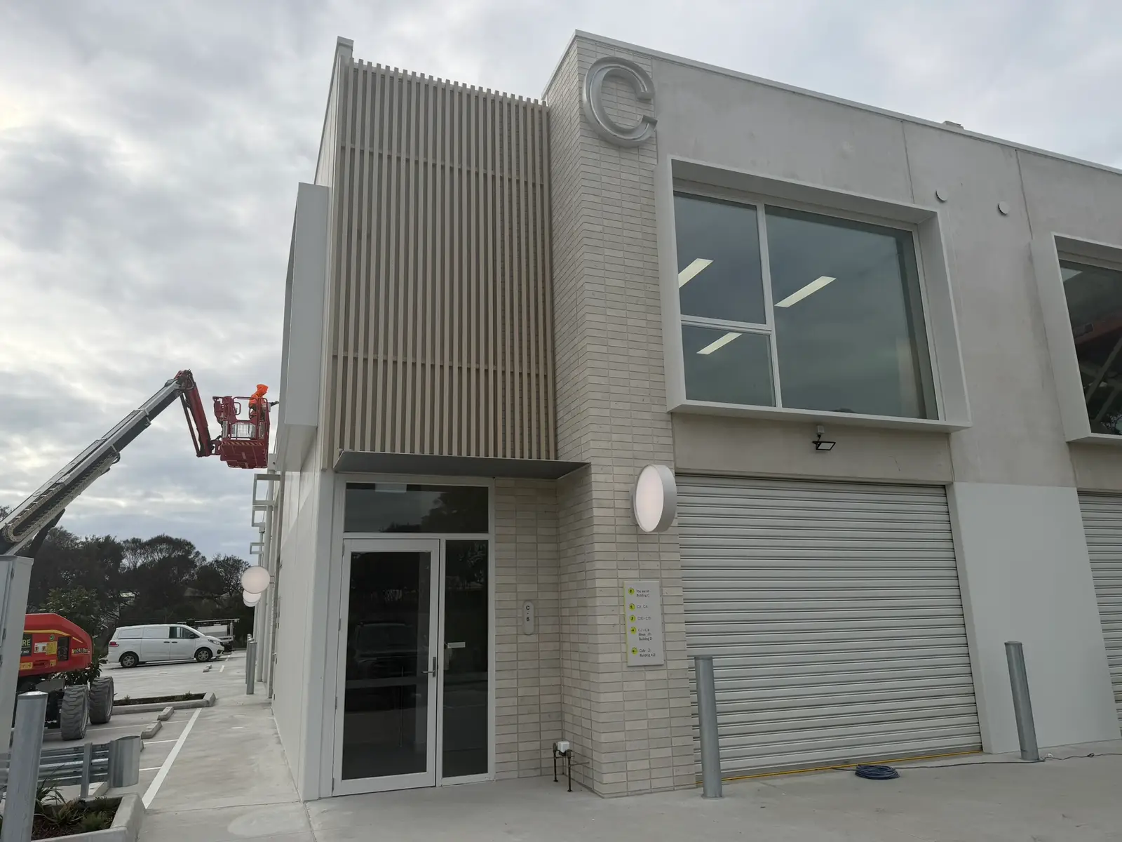 A boom lift and a worker in high-vis finishing the upper facade of Building C at Free Form, Mornington, at dusk