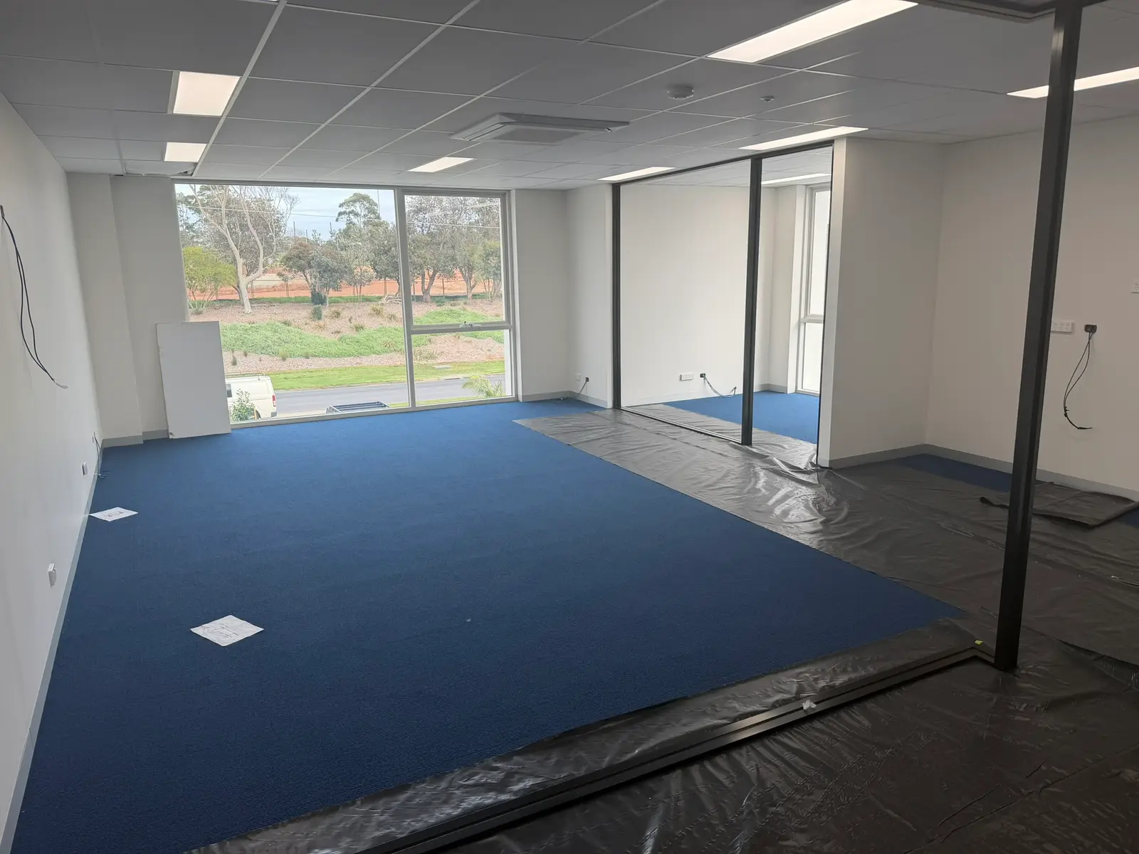 Interior of Agile IT's new office at Free Form, Mornington during fit-out, blue carpet laid, glass partitions in, a large window looking out to the road and landscaping