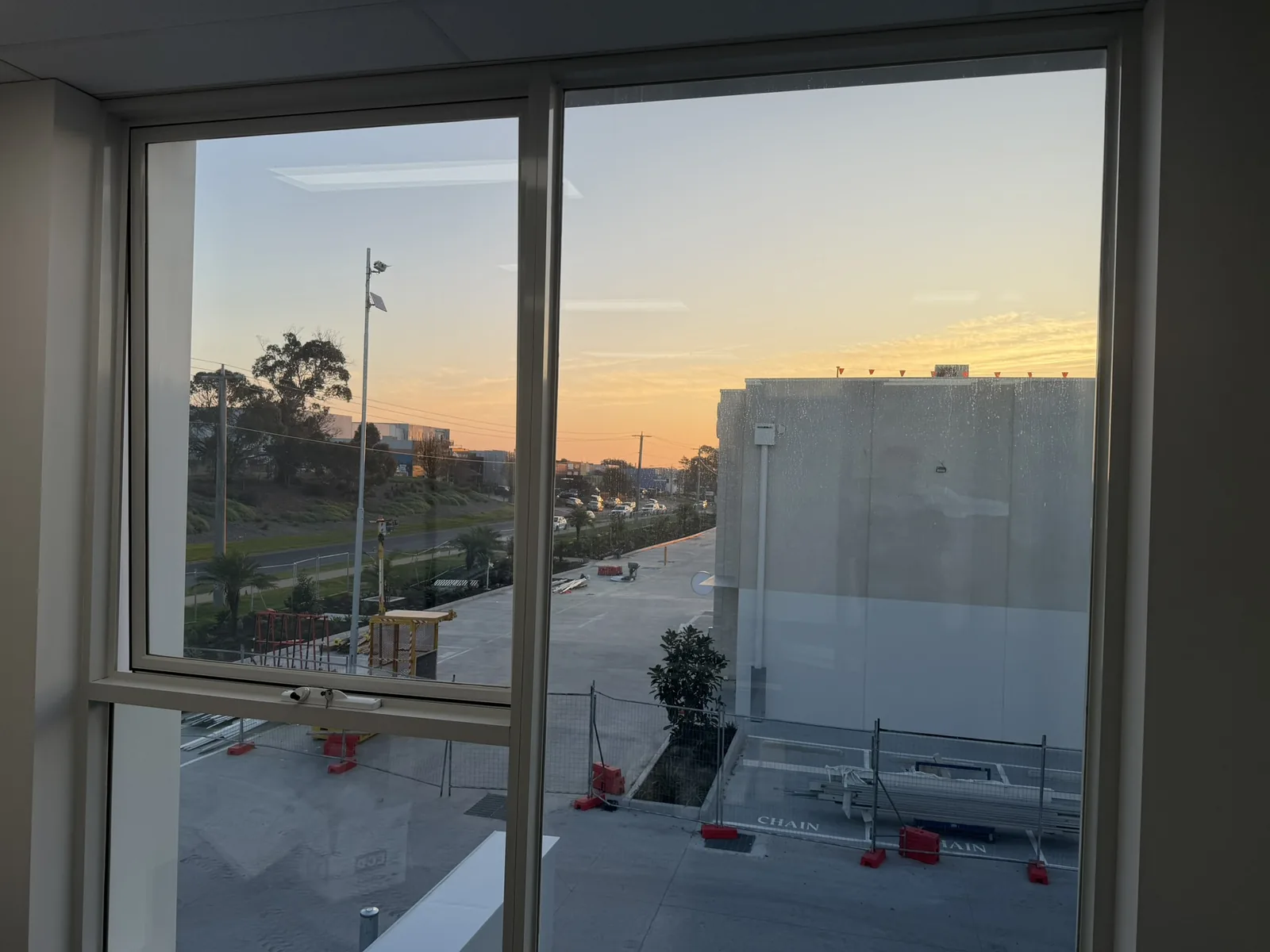 The view west from an upstairs window at Free Form, Mornington at sunset, an orange sky over the road, palms and the neighbouring buildings