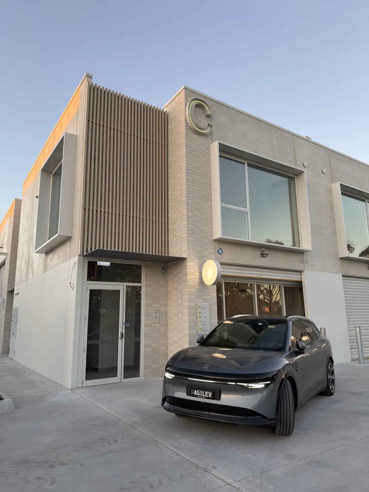 Building C at Free Form, Mornington at dusk, the illuminated C sign glowing above the entrance and the Agile IT Zeekr electric car, plate AGILEV, parked out the front