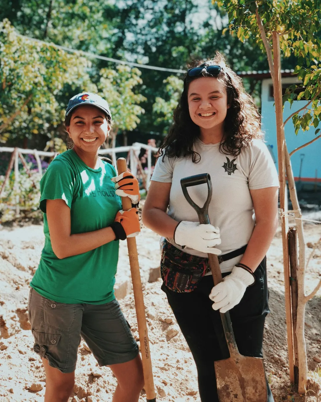 Two young volunteers smiling with shovels at a community building project, the kind of hands-on work the organisations we support make possible.
