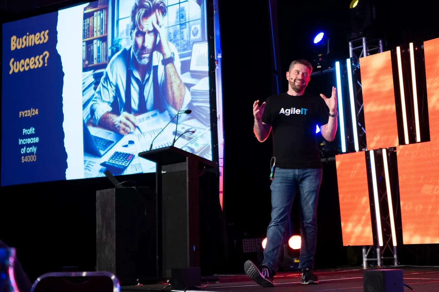 Linden Jackson on stage at SMBiT Professionals in October 2024, beside a slide reading 'Business Success? FY23/24 Profit Increase of only $4000'.
