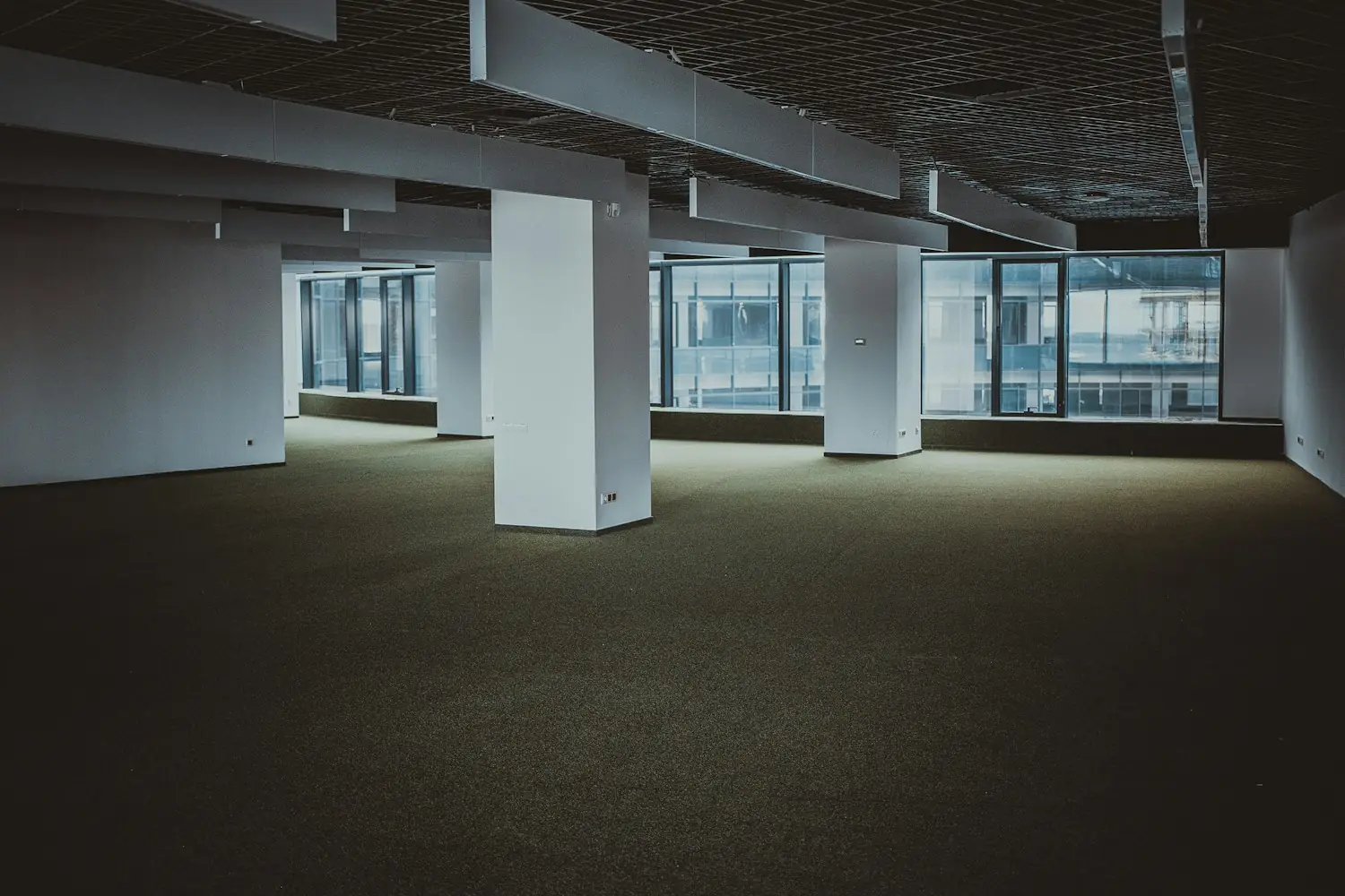 An empty, newly fitted office floor with bare carpet and columns, waiting for the cabling, network and people to arrive