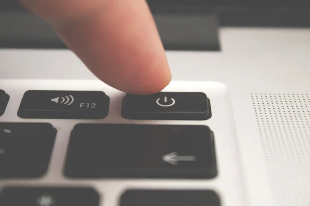 A finger pressing the power button on a laptop keyboard.